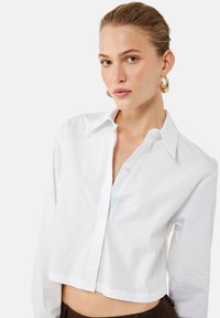 Hvid kortærmet button-up skjorte med klassisk krave, der har lange ærmer og et glat, let stof. Ingen synlige mønstre eller detaljer.