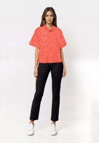 Koral kortermet skjorte med krage, med broderte mønstre. Sammen med svarte slim-fit bukser og hvite sneakers.