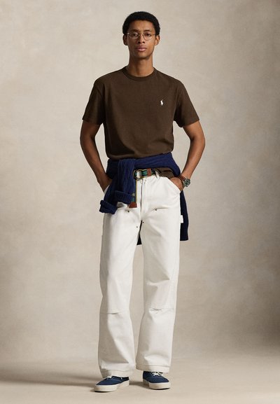 Tricou maro din bumbac, pantaloni albi cu croială largă, pulover bleumarin legat în talie, adidași albaștri, ochelari rotunzi și un ceas de mână.