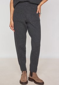 Pantaloni in maglia grigio carbone con un taglio affusolato, dotati di due tasche frontali e una vita a coste. Abbinati a stivaletti alla caviglia marroni.