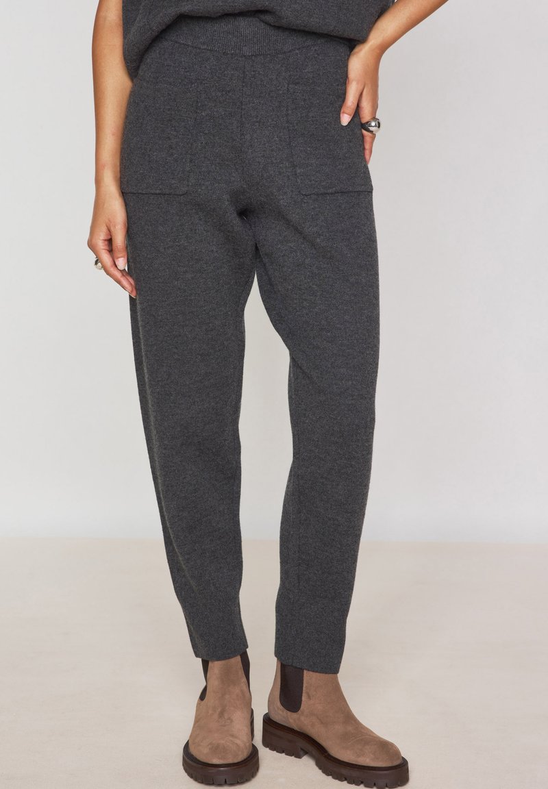 Pantaloni in maglia grigio carbone con un taglio affusolato, dotati di due tasche frontali e una vita a coste. Abbinati a stivaletti alla caviglia marroni.
