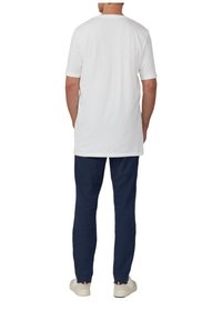 Weißes Baumwoll-T-Shirt mit kurzen Ärmeln und Rundhalsausschnitt, getragen mit marineblauen Hosen und weißen Schuhen, von hinten betrachtet.