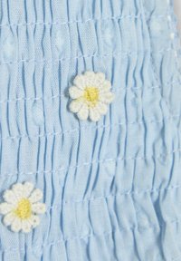 Lichtblauwe, geraffineerde stof met kleine, geborduurde witte madeliefjes met gele centra. Textuur met verhoogde stippen en plooien.