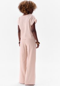 Jasnoróżowa bluzka w paski z krótkimi rękawami, zestawiona z szerokimi różowymi spodniami. Miękka tekstura materiału, swobodny fason z luźnym krojem.