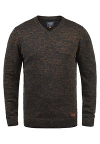 Pull en v marron foncé avec de subtils éclats de marron clair, poignets et ourlet côtelés. Présente un petit patch en cuir logo sur le bord inférieur.