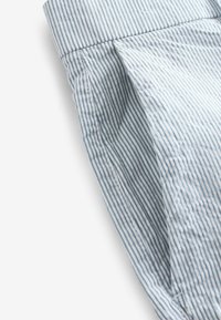 Tejido a rayas azul claro y blanco con una textura suave. Presenta un pliegue y un cuello doblado. Enfocado en líneas limpias y un patrón sutil.