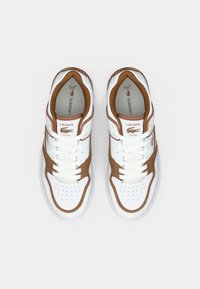 Λευκά και καφέ αθλητικά παπούτσια Lacoste με κορδόνια, διάτρητη μύτη και λογότυπο στη γλώσσα και στην εσωτερική σόλα, από ψηλά σε λευκό φόντο.