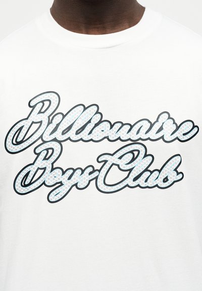 Κοντινό πλάνο ενός λευκού μπλουζάκι με την επιγραφή "Billionaire Boys Club" γραμμένη με μεγάλο, διακοσμητικό γραφικό στυλ στη μέση του στήθους.