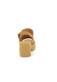 Sandalias de tacón de ante marrón con plantilla acolchada, correa ajustable en el tobillo y suela texturada beige. Enfocadas en la simplicidad y la comodidad.