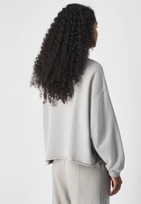 Lichtgrijze, oversized sweatshirt met verlaagde schouders, ruwe zoom en zachte textuur, gecombineerd met bijpassende broek. Achteraanzicht weergegeven.
