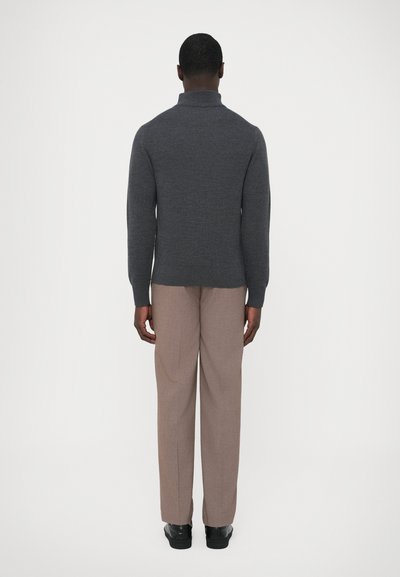 Camisola cinzenta de malha com gola alta, design ajustado, textura subtil. Combinada com calças castanho claro e sapatos pretos. Visual simples e monocromático.