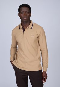 Polo à manches longues beige avec un col marron foncé et des détails rayés subtils, présentant un petit logo brodé sur la poitrine.