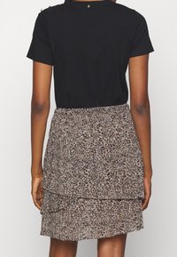 Zwarte top met korte mouwen en een gerimpelde zoom, gecombineerd met een gelaagde dierenprint rok met ruches in bruintinten en crème.