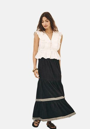 Blusa blanca con volantes y escote en V profundo, combinada con una falda maxi negra con capas escalonadas y un detalle de trenzado en el dobladillo.