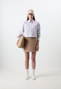 Gestreepte blouse in blauw en wit, beige rok, beige pet, bruine gestructureerde tas en witte sneakers met groene accenten.