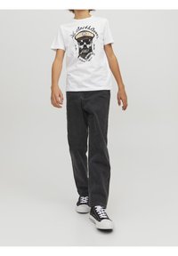 Camiseta blanca de algodón con estampado gráfico que presenta una calavera y un sombrero, combinada con jeans de mezclilla negros y zapatillas negras con suelas blancas.