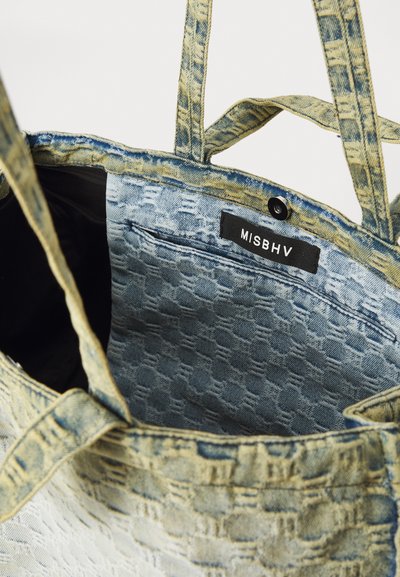 Geantă din denim cu textură țesută albastră și bej, având un etichetă neagră inscriptionată "MISBHV" și un buzunar interior.