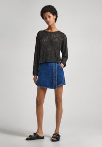 Svart stickad långärmad topp med ett löst, texturerat mönster; blå denimwrapkjol; svarta halkskor med nitar.