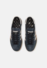 Zapatillas de gamuza azul con cordones negros y acentos de logo blancos. Cuentan con suelas de goma y un forro interior con patrón.