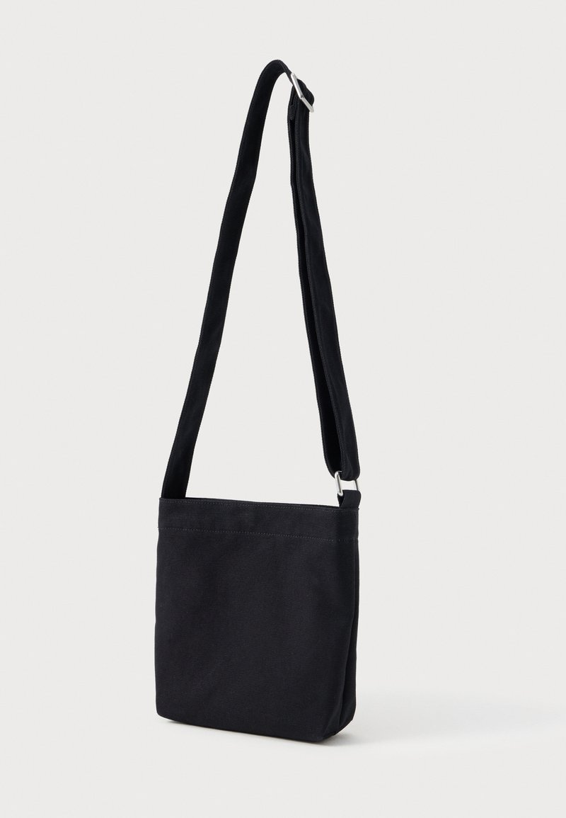Black fabric crossbody bag with adjustable strap and silver buckle on a white background.