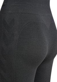 Nahaufnahme von schwarzen nahtlosen Leggings, die strukturierte Muster sowie Rippungen im Taillen- und Oberschenkelbereich zeigen.
