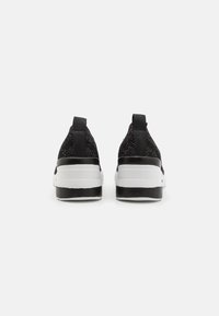 Svarta nätträningsskor med vitt mellansula och svart yttersula. Har två dragflikar baktill för enkel påtagning.