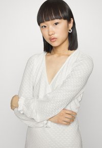 Vestido branco texturizado com decote em V, mangas bufantes e punhos franzidos, apresentando um padrão subtil em toda a peça.