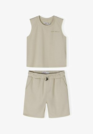 Beżowy bezrękawnik typu crop top z haftowanym napisem, sparowany z dopasowanymi szortami z elastycznym pasem i bocznymi kieszeniami. Wykonane z miękkiego materiału bawełnianego.