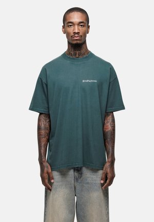 Zielony, oversize'owy t-shirt bawełniany z okrągłym dekoltem i krótkimi rękawami. Posiada biały nadruk na piersi. W połączeniu z jasnoniebieskimi dżinsami.