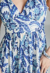 Robe bleue et blanche à motif, avec un design enveloppant, comportant des motifs floraux, des rayures verticales et une texture fluide.