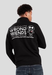 Sudadera negra con cuello alto. Presenta un gran diseño gráfico en blanco en la parte posterior con texto y un personaje de dibujos animados. Textura suave.
