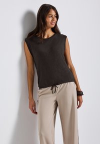 Tmavě šedý top bez rukávů s kulatým výstřihem a stahovací spodní částí. V kombinaci s béžovými, volně střiženými kalhotami. Hladký textilní povrch.
