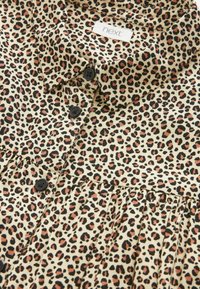 Leopardikuosi paita vaalealla taustalla, mustia ja ruskeita laikkuja, napitettava etuosa ja poimutettu yksityiskohta helmasssa. Valmistettu kevyestä kankaasta.