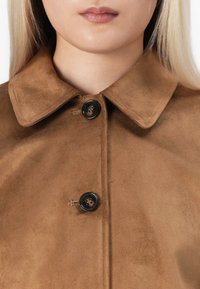 Cappotto in suede marrone con colletto classico, due bottoni neri e una superficie liscia, che mette in risalto un design pulito e semplice.