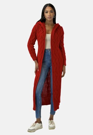 Cárdigan largo de punto rojo con capucha, con un patrón de trenzado y diseño de abertura frontal. Combinado con jeans azul claro y zapatillas blancas.