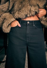 Sorte jeans med høj talje og lige ben, med sidelommer og en sølvfarvet knappelukning. Stoffet har en glat tekstur.