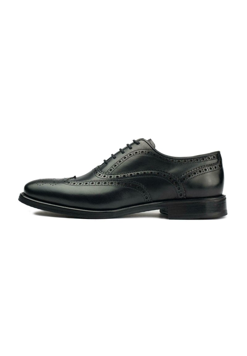 Black leather dress shoe with brogue detailing, lace-up closure, rounded toe, and a low stacked heel. Smooth finish with accent stitching.