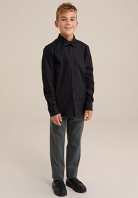 Chemise noire à manches longues avec boutons et nœud papillon, associée à un pantalon gris et des chaussures noires. Tissu lisse, coupe ajustée et design classique.