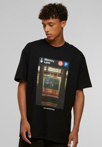 Sort t-shirt med et grafisk motiv af et metrovindue med graffiti og skiltning, der læser "Memory Lane" og "UP," med hvid tekst nedenfor.