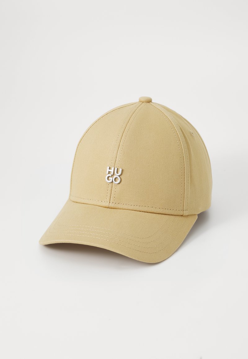 Béžová baseballová čiapka so štruktúrovaným dizajnom, s zaoblenou korunou a zakriveným brímom. Strieborné logo "HUGO" vpredu.