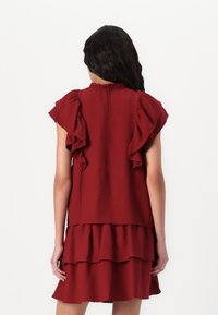 Robe rouge à volants avec une jupe à plusieurs niveaux, fabriquée en tissu texturé. Elle présente des manches courtes et une fermeture au dos.