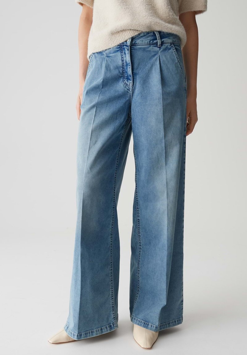 Hoge taille, wijde blauwe jeans met plooien aan de voorkant, gedragen met een romige fuzzy trui met korte mouwen en beige puntige schoenen.