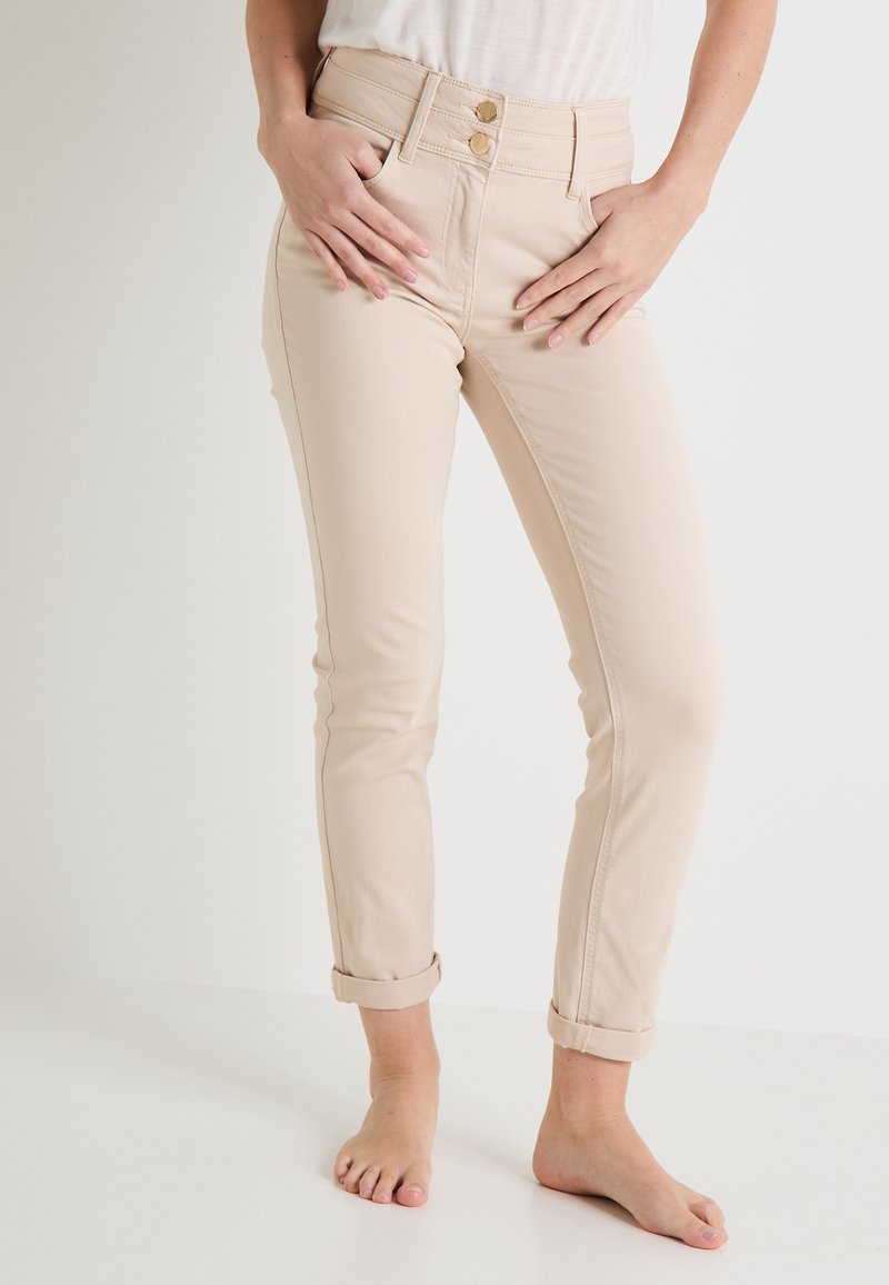 Pantalones beige de cintura alta, con dos acentos de botones dorados y puños enrollados. Fabricados con una tela suave y elástica para mayor comodidad.