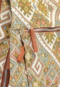 Tkaná taška se geometrickým vzorem v tlumených odstínech zelené, žluté a modré, s koženými akcenty a zipovým uzávěrem. Texturovaná látka.