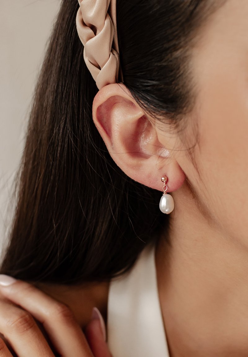 Perlen Tropfen Ohrringe mit einem runden Metallakzent. Die Perlen sind weiß und oval geformt, hängend von einem goldfarbenen Haken.