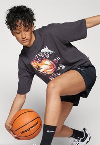 Camiseta gráfica negra con un diseño de baloncesto y llamas, combinada con pantalones cortos atléticos negros y un balón de baloncesto. Zapatillas bajas y calcetines negros.