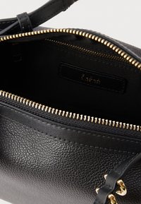 Melna ādas rokas soma ar teksturētu virsmu, zelta tonēta rāvējslēdzēja un melnas auduma iekšpusi ar zīmola etiķeti.