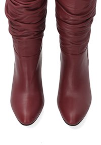 Burgundské kožené vysoké boty po kolena s hladkým povrchem, špičatou špičkou a nařaseným designem kolem holeně. Černá podrážka.