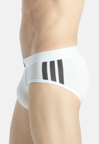 Bañadores de hombre blancos con una cinturilla sólida y tres rayas negras en el lado izquierdo, hechos de una tela suave y elástica.