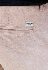 Svijetlo ružičaste hlače od teksturiranog materijala. Imaju diskretni stražnji džep s bijelom etiketom na kojoj piše "JACK & JONES EST. 1990."
